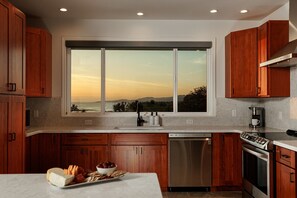 A modern kitchen with wooden cabinets, a stainless steel dishwasher, and a large window overlooking a scenic view.