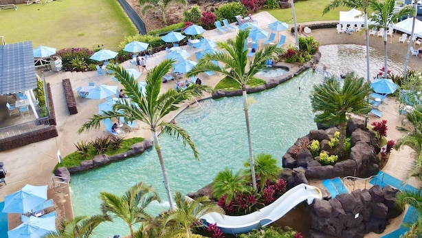 Un resort con piscina, sillas de descanso, sombrillas y un tobogán.