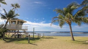 Una torre de salvavidas en una playa con palmeras y cielo azul despejado.