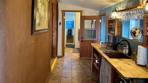 A hallway with a wooden door leading to a room, a tiled floor, and a kitchen area with a wooden countertop and various items. - Anam Cara Vineyard. Romantic Vineyard Cottage with sweeping views (Elgin)