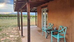 A covered outdoor seating area with a table and chairs, a door, and a view of a vineyard. - Anam Cara Vineyard. Romantic Vineyard Cottage with sweeping views (Elgin)