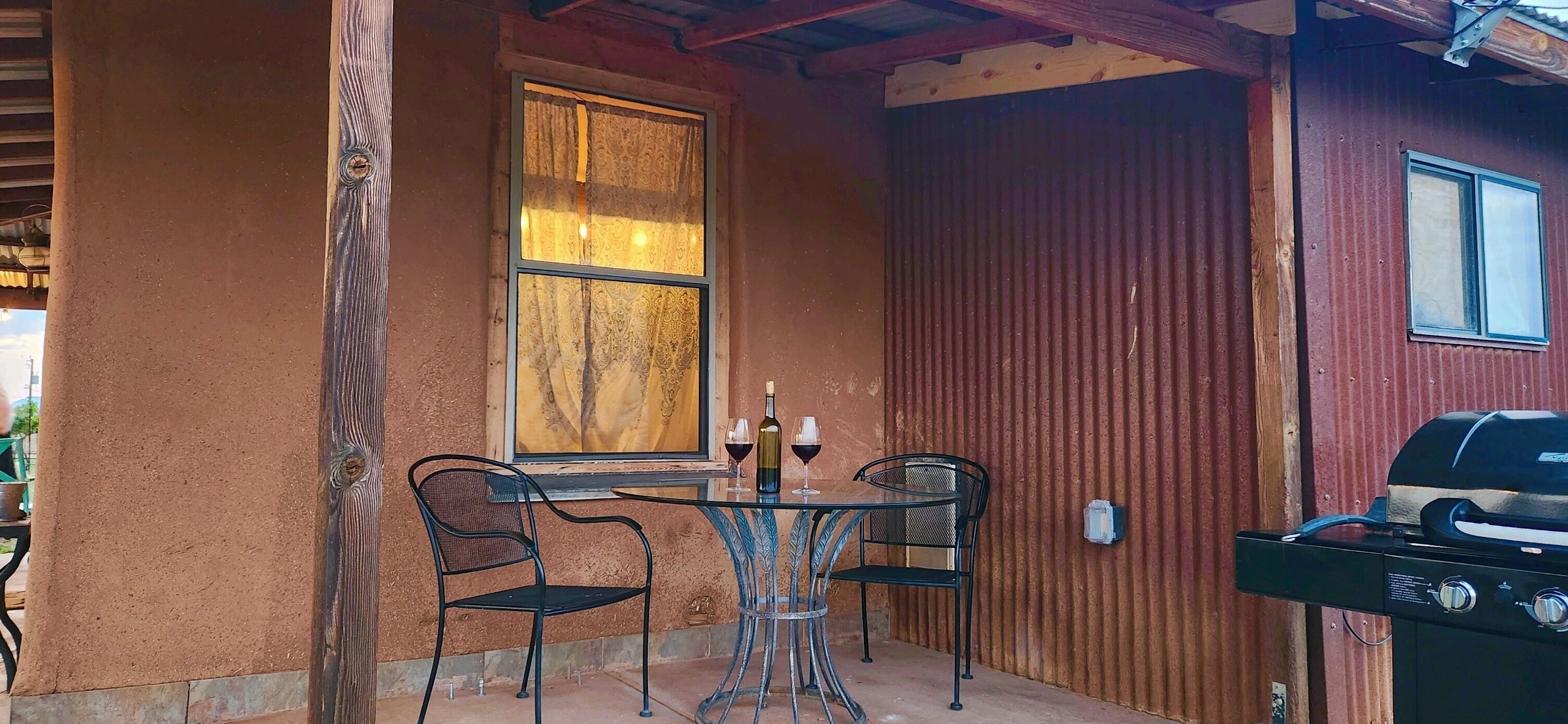 Une terrasse extérieure avec une table et des chaises, une fenêtre avec des rideaux et un barbecue.
