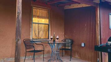 Une terrasse extérieure avec une table et des chaises, une fenêtre avec des rideaux et un barbecue.