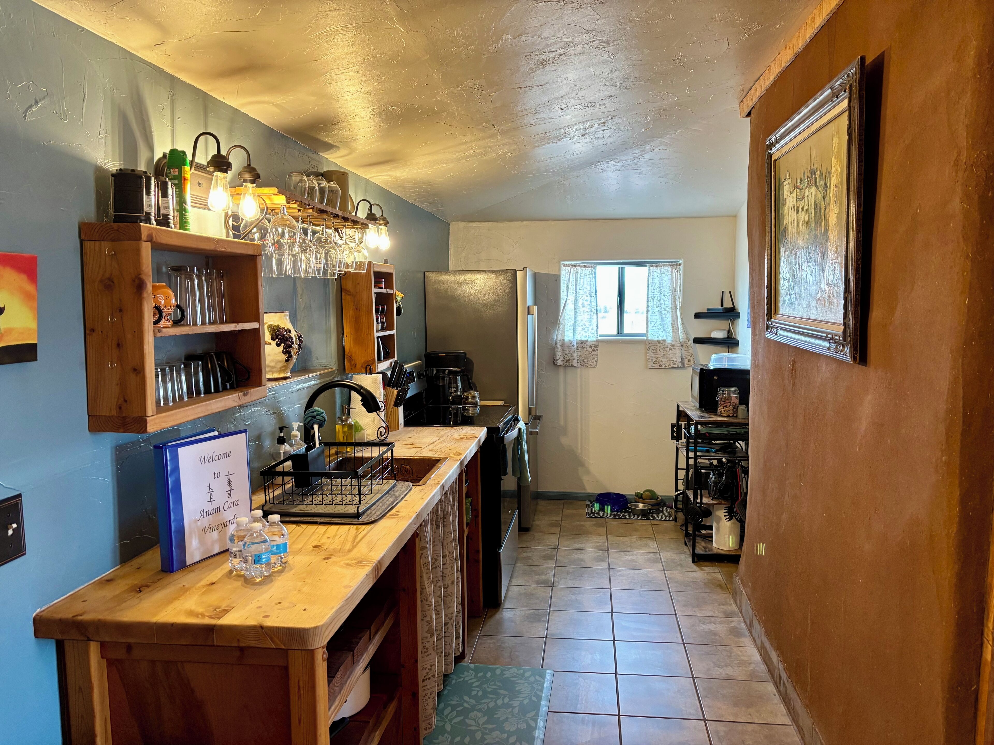 Una cocina con armarios de madera, una cafetera y un ventanal con cortinas.