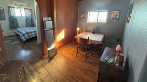 A cozy room with a wooden ceiling, a bed with a checkered bedspread, a dining table with chairs, and a small kitchen area. - Anam Cara Vineyard. Romantic Vineyard Cottage with sweeping views (Elgin)