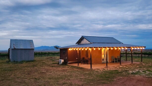 A rustic cabin with a covered patio and string lights, surrounded by a vineyard. - Anam Cara Vineyard. Romantic Vineyard Cottage with sweeping views (Elgin)