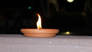 Ett tänt ljus i en terrakottafärgad ljusstake som står på en stenkant.