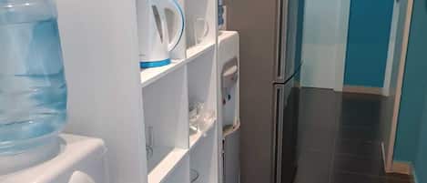 A compact kitchen with a refrigerator, microwave, water dispenser, and a water cooler.