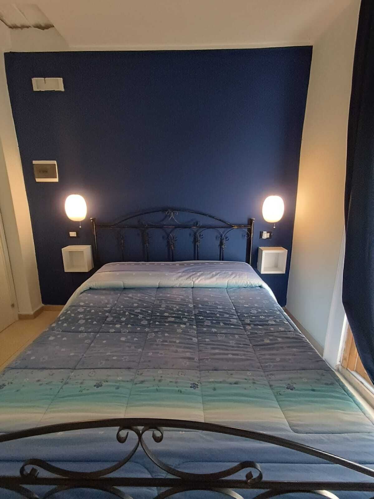 Una cama con cabecera azul, dos lámparas de noche y una colcha estampada.