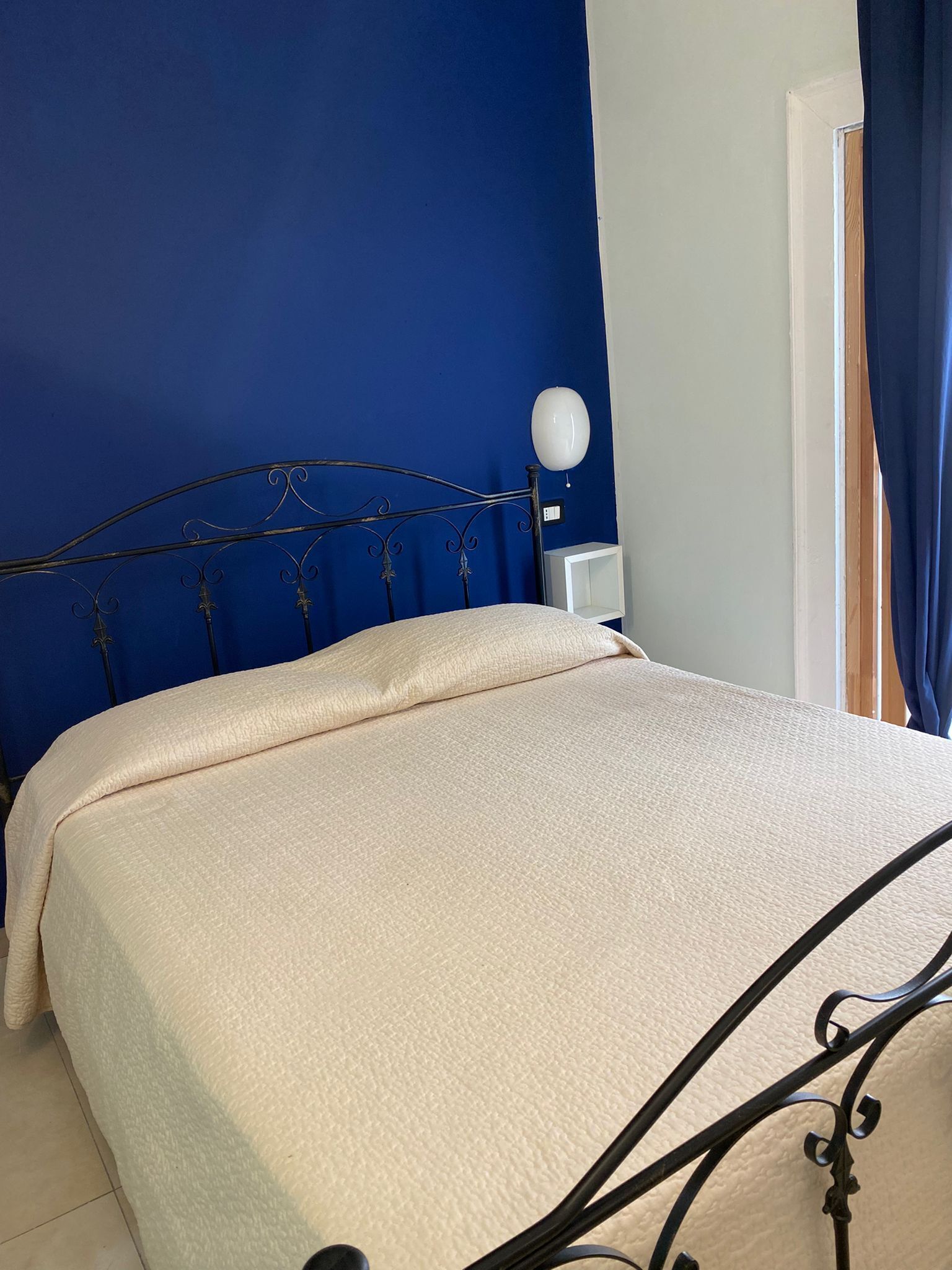 A bed with a metal frame and a beige bedspread in a room with blue walls and a white nightstand.