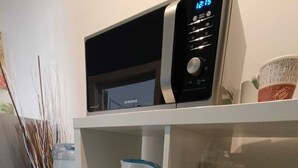Ett köksutrymme med en vattenautomat, vattenkokare, mikrovågsugn och hyllor med glas och tallrikar.
