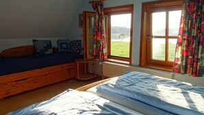 A bedroom with two beds, a window with curtains, a radiator, and a small table. - Vacation home with large meadow on nature reserve lake (Petershagen)