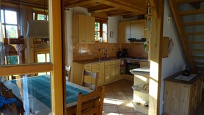 A cozy kitchen with wooden cabinets, a sink, and a stove. There is a dining table with chairs and a window providing natural light. - Vacation home with large meadow on nature reserve lake (Petershagen)