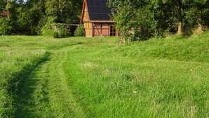 A rural house with a sloped roof, surrounded by lush greenery and a grassy field. - Vacation home with large meadow on nature reserve lake (Petershagen)