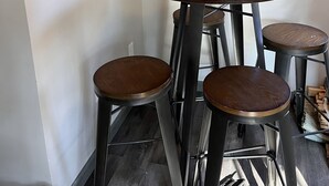 Un coin repas avec une table ronde en bois, quatre tabourets et une horloge murale.