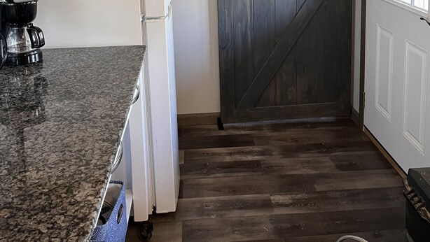 A kitchen with a granite countertop, a white refrigerator, a coffee maker, and a wooden door.