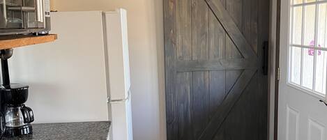 Cocina con encimera de granito, refrigerador blanco, cafetera y puerta de madera.