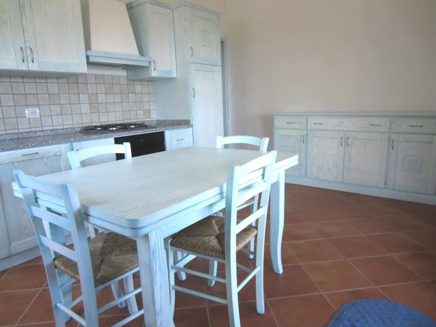 Une cuisine avec des meubles blancs, un plan de travail carrelé, une cuisinière et une table à manger avec des chaises.