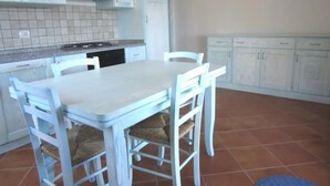 Une cuisine avec des meubles blancs, un plan de travail carrelé, une cuisinière et une table à manger avec des chaises.