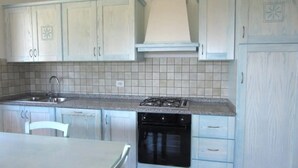 Une cuisine avec des meubles blancs, une cuisinière à gaz, un lave-vaisselle et un dosseret carrelé.