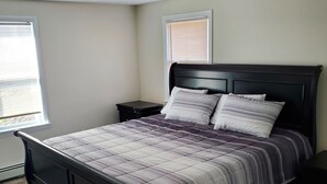 Une chambre à coucher comprenant un lit, des tables de chevet, une fenêtre avec des stores et un luminaire au plafond.
