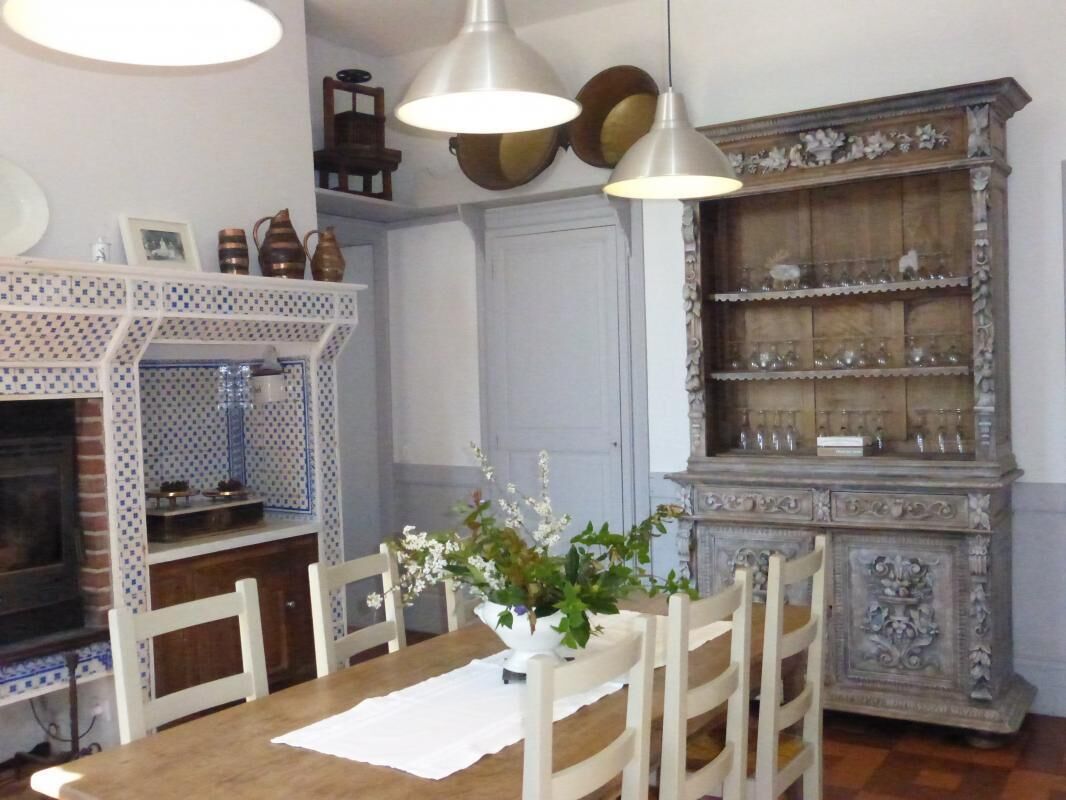Een eetgedeelte met een houten tafel, witte stoelen, een witte tafelkleed, een vaas met bloemen en een decor kast met glaswerk.