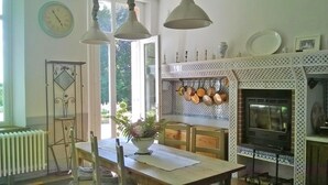 A kitchen with a dining table, hanging pots, a clock, and a fireplace. - Family chateau in the middle of its large wooded park. (Hugleville-en-Caux)