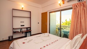 Une chambre d’hôtel équipée d’un lit, d’un bureau, d’une chaise, d’une petite poubelle et d’une porte-fenêtre coulissante donnant sur un espace extérieur.