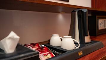Una estación de café con una cafetera, dos tazas blancas y sobres de café instantáneo.