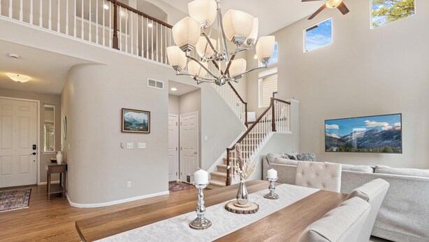 A spacious living room with a wooden dining table, white sofas, a staircase, and a large window with a mountain view. - Epic 140 inch TV Wall + Game Consoles Galore (Commerce City)