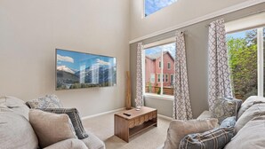 A living room with a large window, a mounted TV, and a wooden bench. - Epic 140 inch TV Wall + Game Consoles Galore (Commerce City)