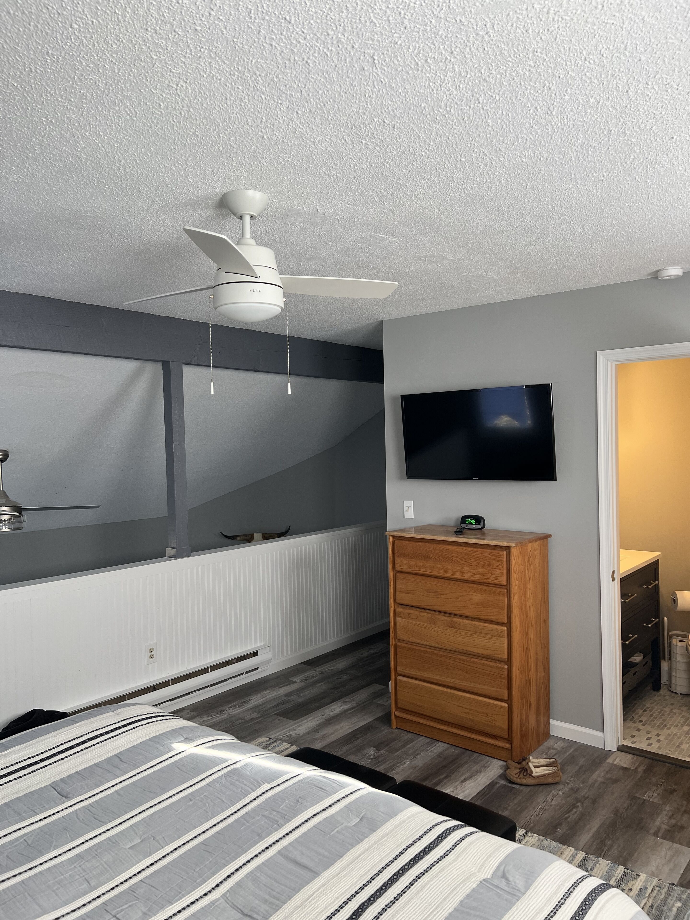 A bedroom with a bed, a wooden dresser, a ceiling fan, a TV, and a radiator.