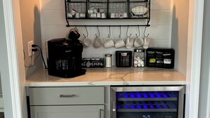 A compact coffee station with a coffee sign, a coffee machine, a refrigerator with blue lighting, and a shelf with mugs and cups.