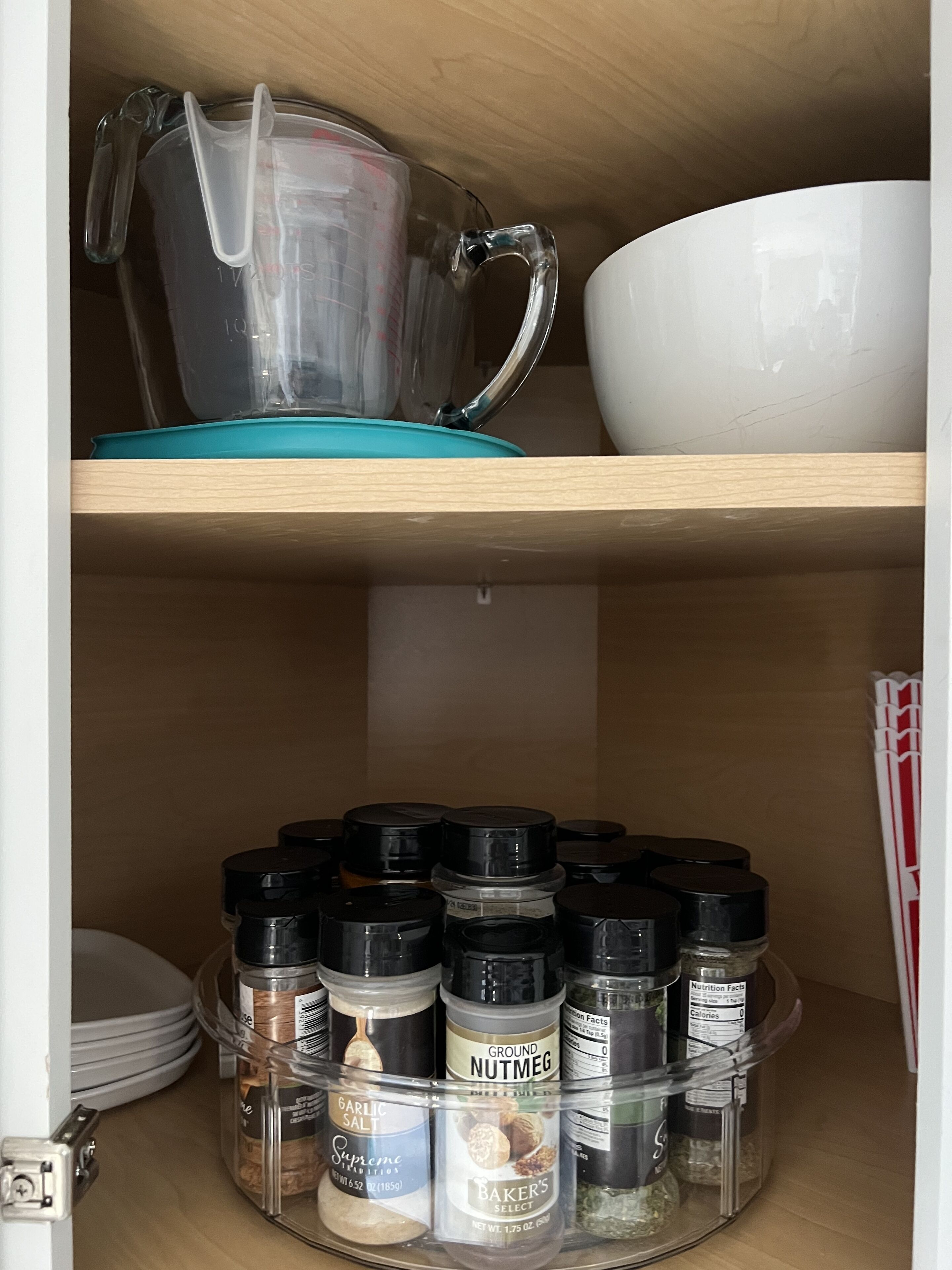 A kitchen shelf with a measuring cup, a white bowl, and various spice containers.
