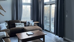 A modern living room with a brown leather sofa, a wooden coffee table, and a large window with dark curtains.