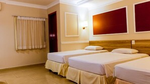 Habitación de hotel con dos camas individuales, cabecero de madera, ventana con cortinas y una lámpara fijada a la pared.