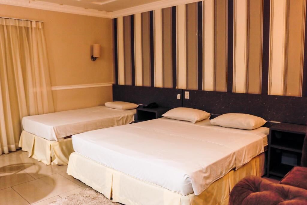 Une chambre d’hôtel avec deux lits simples, une tête de lit sombre, une table de chevet et un fauteuil rouge.