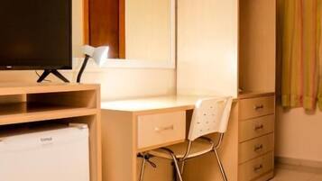 Une chambre d’hôtel de taille réduite, comprenant un lit simple, un bureau avec une chaise, une télévision, un mini-réfrigérateur et une armoire.