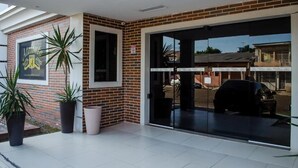 Entrada de un edificio con puerta de vidrio, plantas en macetas y pared de ladrillo.