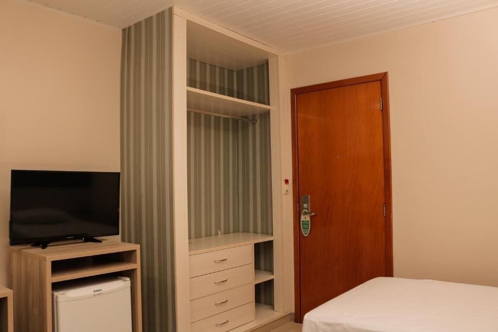 A bedroom with a TV, a mini-fridge, a wardrobe, and a bed.