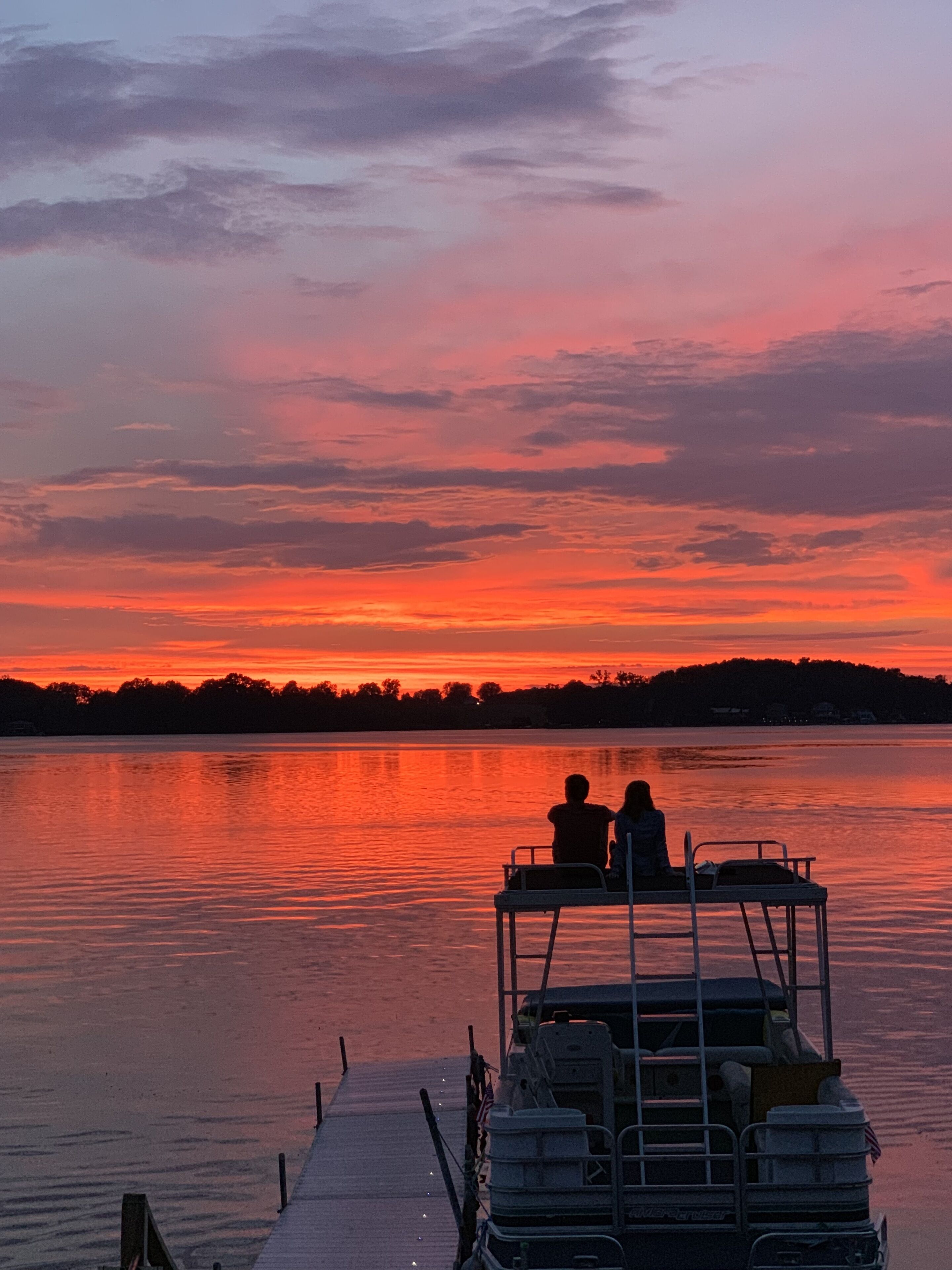 Un coucher de soleil sur un lac paisible, avec un quai et un bateau.
