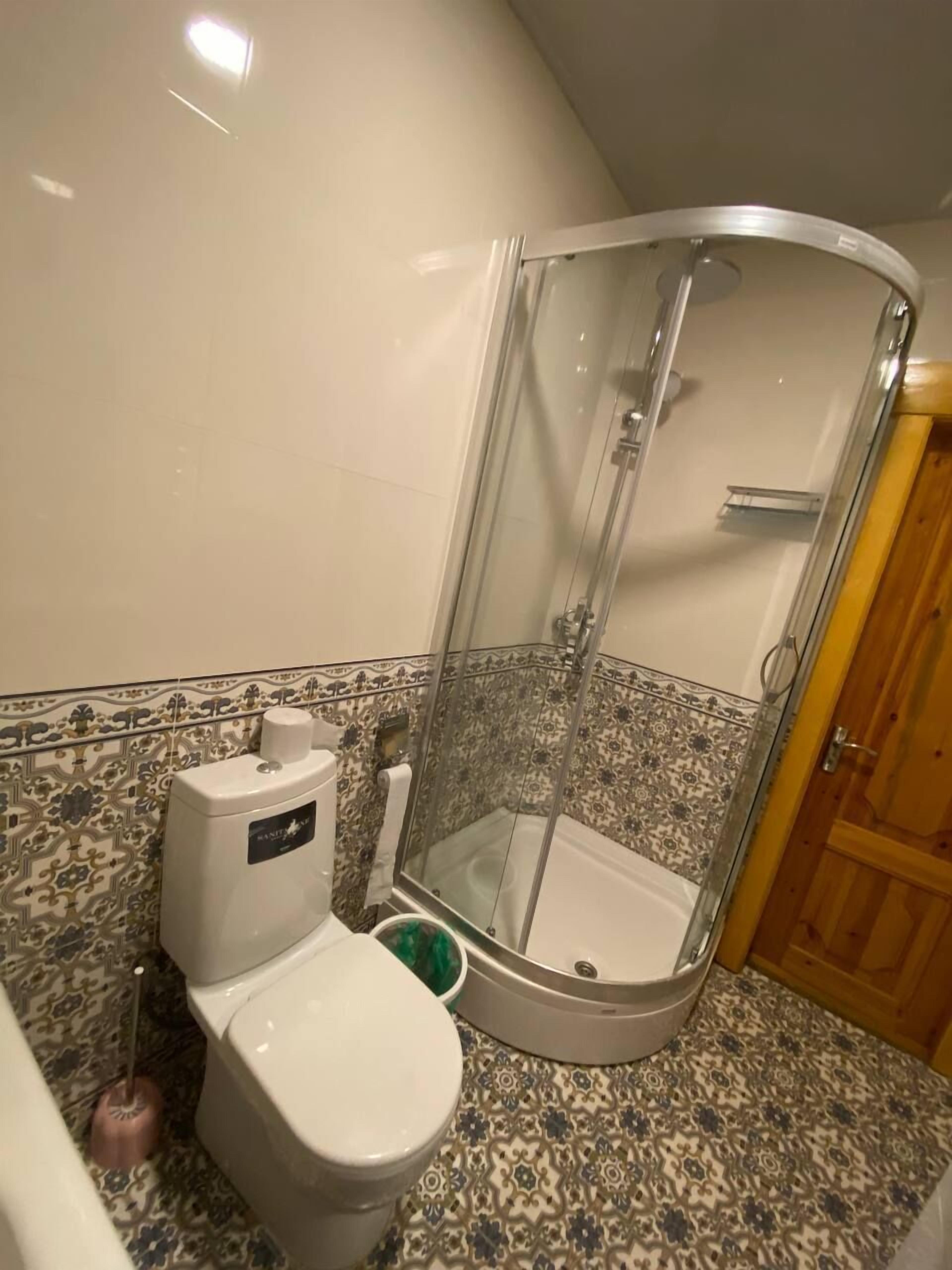 Un baño con cabina de ducha, inodoro y suelo estampado.