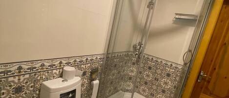 Un baño con cabina de ducha, inodoro y suelo estampado.