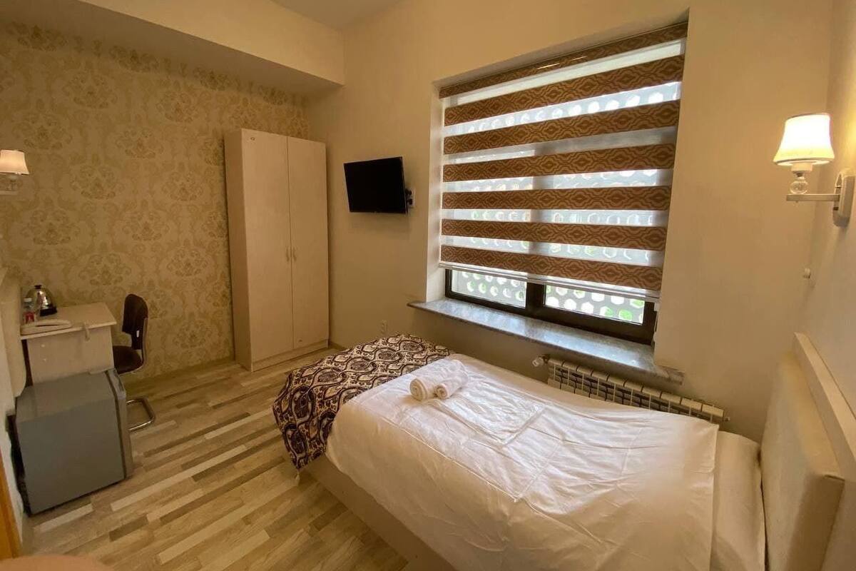 Un dormitorio con cama, escritorio, silla, armario y ventana con persianas.