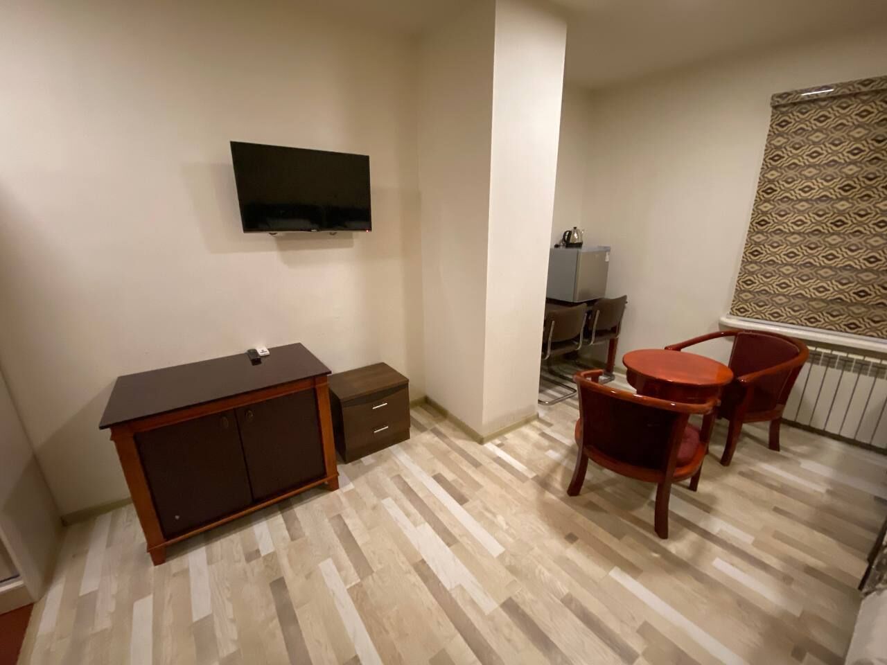 A small room with a wooden desk, a television mounted on the wall, and two red chairs.