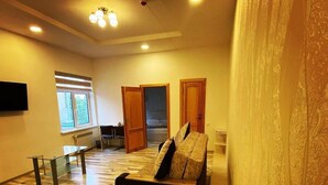 A spacious living room with a wooden floor, a sofa, a glass coffee table, and a TV mounted on the wall. - Hotel Diyor (Samarkand)