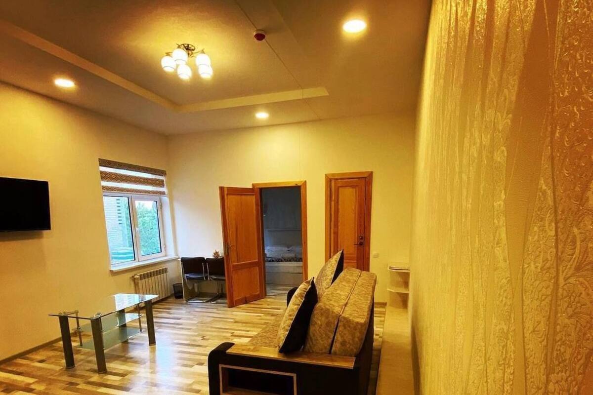 Un salón espacioso con suelo de madera, un sofá, una mesa de centro de cristal y un televisor fijado en la pared.