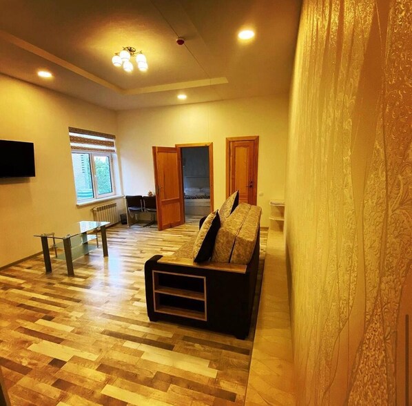 A spacious living room with a wooden floor, a sofa, a glass coffee table, and a TV mounted on the wall. - Hotel Diyor (Samarkand)