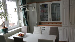 Eine moderne Küche mit weißen Schränken, einem Esstisch und Stühlen. Auf der Fensterbank steht ein Blumentopf und auf dem Tisch eine Obstschale.