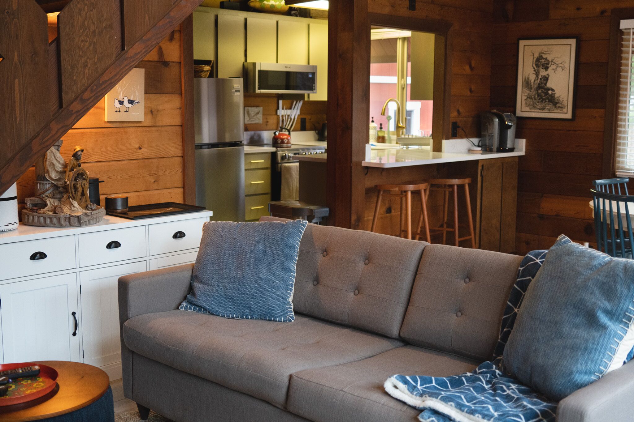 A cozy cabin interior with a sofa, kitchen area, and wooden walls.